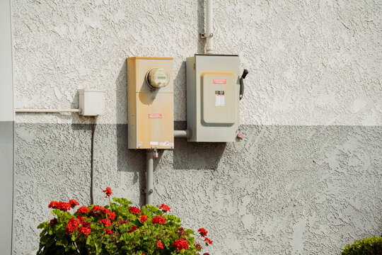 Outdoor electrical meter and breaker box mounted on a textured wall with flowers