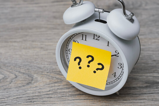 Business problem and confusion concept with questions on adhesive paper. White clock on wooden desk symbolizes deadline pressure, lost time or searching for answers in career and education.