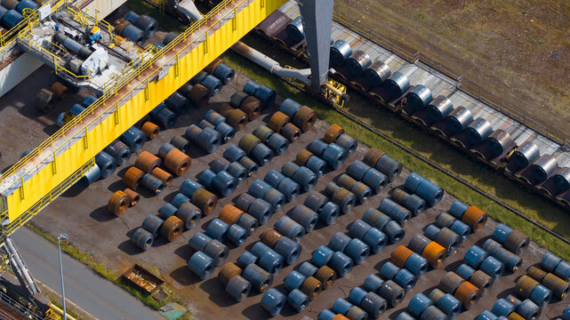 Aerial view of the Tata Steel plant featuring rows of large steel coils and industrial machinery under bright daylight in Velsen-Noord, Noord-Holland, Netherlands.