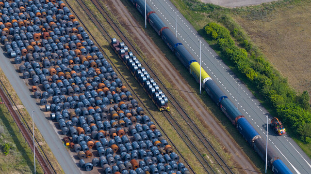 Aerial view of the Tata Steel industrial site featuring rows of steel coils, railway tracks with a freight train, and a road in Velsen-Noord, Noord-Holland, Netherlands.