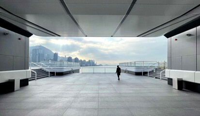 Obraz premium Lone figure walks on modern rooftop terrace overlooking city skyline and ocean
