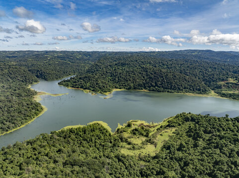 Aerial view of Chemosusu Dam surrounded by dense tropical forest and rolling hills under a bright blue sky with white clouds Chemosusu, Baringo County, Kenya.