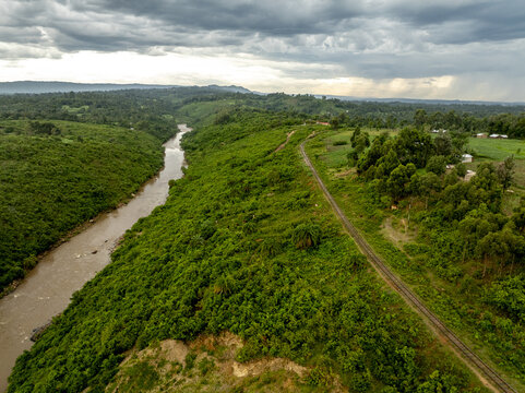 Aerial view of the Nzoia River valley and a railway track winding through lush green hills under a cloudy sky Webuye, Bungoma County, Kenya.