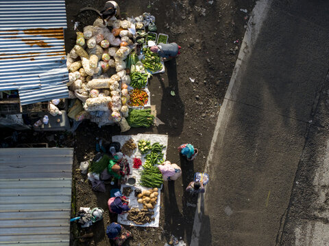 Aerial view of Pasar Kembang Klaten traditional market with vendors selling fresh vegetables on the ground next to corrugated metal roofs and a road in Klaten, Central Java, Indonesia.