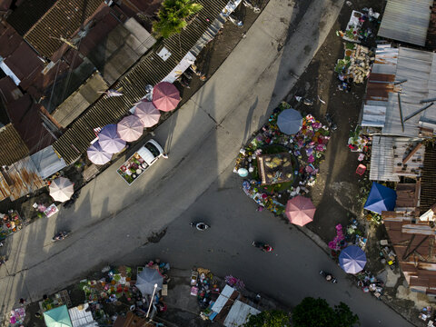 Aerial view of Pasar Kembang Klaten traditional market with colorful umbrellas, a white truck, and motorcycles at a street intersection in Klaten, Central Java, Indonesia.
