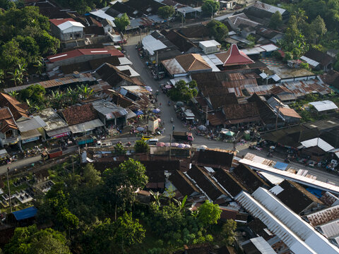 Aerial view of Pasar Kembang Klaten traditional market with busy street stalls, vehicles, and residential rooftops surrounded by lush trees in Klaten, Central Java, Indonesia.