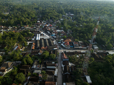 Aerial view of Pasar Kembang Klaten traditional market with a tall telecommunications tower and residential houses surrounded by lush tropical trees in Klaten, Central Java, Indonesia.