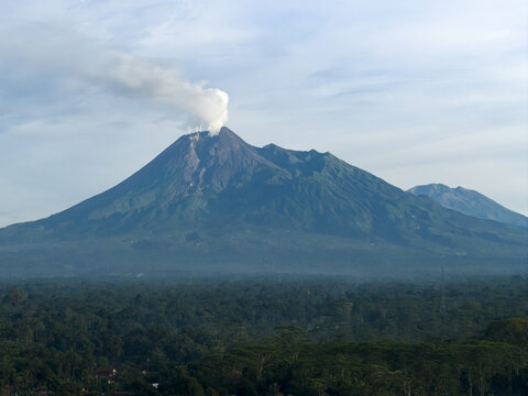 Aerial view of Mount Merapi volcano with smoke rising from the crater above a lush tropical forest Klaten, Central Java, Indonesia.
