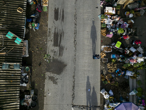 Aerial view of Pasar Kembang Klaten traditional market with vendors, produce stalls, and long shadows on the road in Klaten, Central Java, Indonesia.