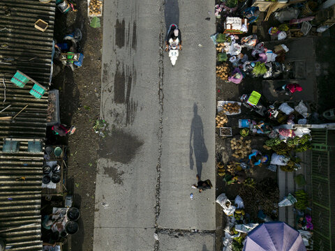 Aerial view of Pasar Kembang Klaten traditional market with a motorbike driving on the road and people walking past stalls in Klaten, Central Java, Indonesia.