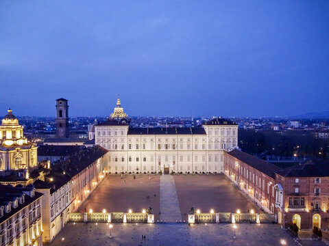 Aerial view of the illuminated Royal Palace of Turin and Piazza Castello with historic domes under a deep blue twilight sky in Turin, Piedmont, Italy.