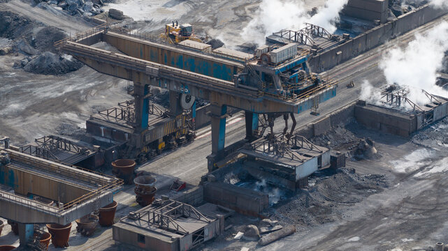 Aerial view of the Tata Steel industrial plant featuring a massive gantry crane, rising steam, and raw material piles in Velsen-Noord, Noord-Holland, Netherlands.