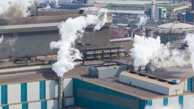 Aerial view of the Tata Steel industrial plant with thick white smoke rising from chimneys and cooling systems in Velsen-Noord, Noord-Holland, Netherlands.