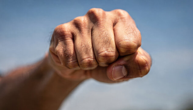 A human hand held in a tight fist against a clear blue sky background