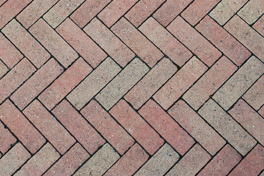 Close-up of some weathered, red Herringbone block paving stones forming a symmetrical zig-zag pattern