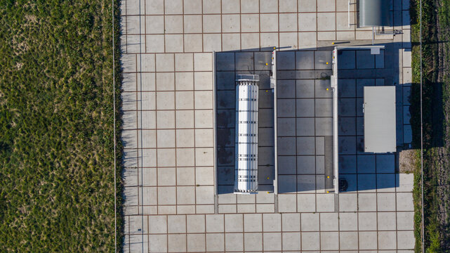 Aerial view of the Erflanden industrial facility featuring a large white storage tank on a concrete tiled platform with utility buildings in Hoogeveen, Drenthe, Netherlands.