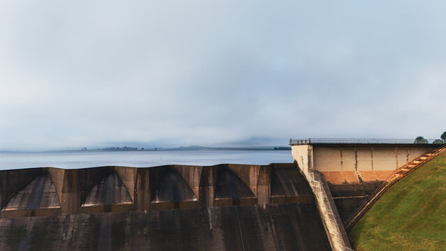 Aerial view of Midmar Dam featuring the concrete spillway, calm water reservoir, and grassy embankment under a misty sky in Howick, KwaZulu-Natal, South Africa.