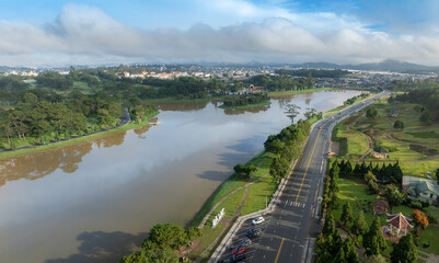 Fototapeta premium An aerial view of Xuan Huong Lake in Da Lat, Vietnam, on a cloudy morning. The lake is surrounded by pine trees and a city skyline.