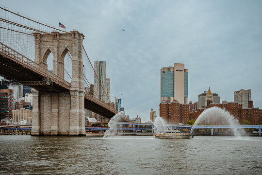 New York, USA, 2 May 2026: FDNY fireboat performing water display salute by Brooklyn Bridge NYC. Fireboat spraying high pressure water jets on East River with Brooklyn Bridge and city skyline