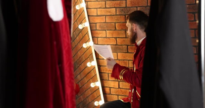Actor with script rehearsing his lines near mirror in dressing room, camera moving right