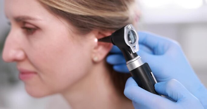 Hearing test. Doctor examining woman's ear with otoscope in clinic, closeup. Camera spinning and moving forward