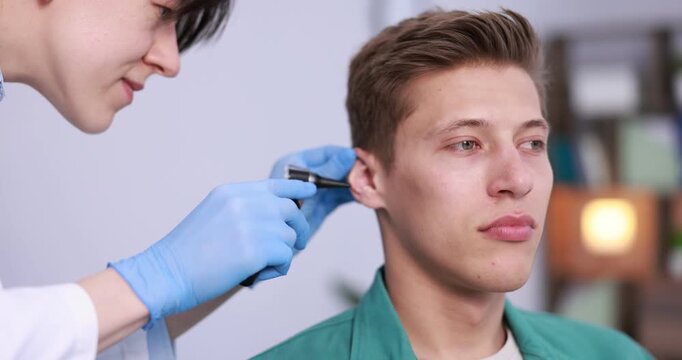 Hearing test. Doctor examining man's ear with otoscope in clinic, closeup. Camera moving left