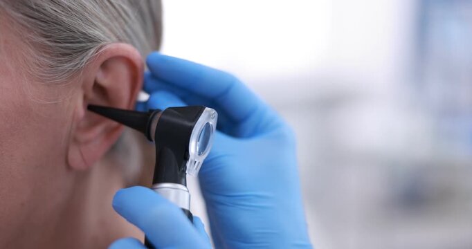 Hearing test. Doctor examining woman's ear with otoscope in clinic, closeup