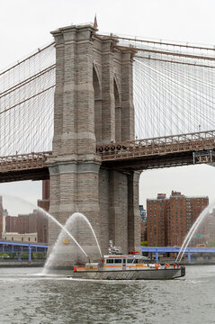 FDNY Fireboat William M Feehan Under Brooklyn Bridge Tower. FDNY fireboat spraying water while passing under the stone tower of the Brooklyn Bridge in NYC.