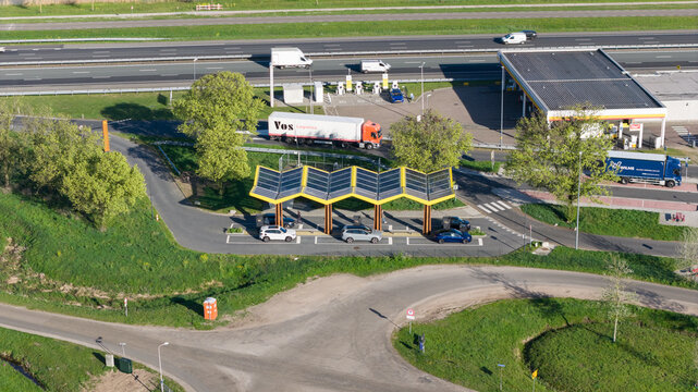 Bant, Netherlands - 23 April 2026: Aerial view of the Fastned Charging Station with its iconic yellow solar roof, electric cars charging, and a busy highway with trucks in the background.