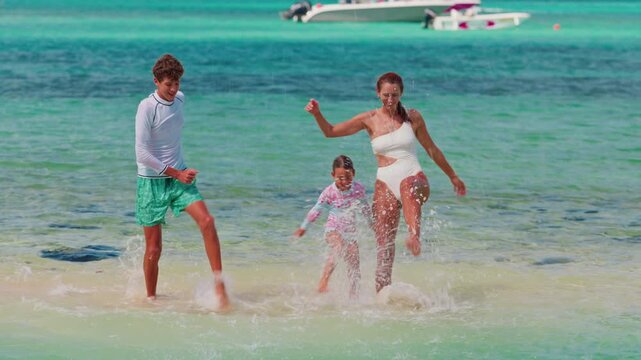 A mother with her children, a young daughter and a teenage son, splash in the crystal clear azure water of the Indian Ocean, having fun on vacation