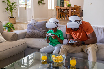 African American father and son playing VR wearing white headsets holding white gamepads at home © wavebreak3
