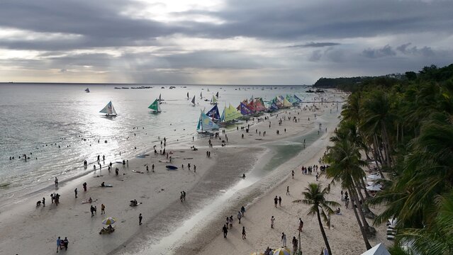 Malay, Philippines - 02 May 2026: Aerial view of Boracay Island featuring the white sand beach, palm trees, and colorful sailboats on the water under a cloudy sky.