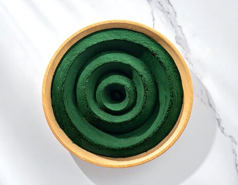 Concentric spirulina powder rings inside wooden bowl on marble background with rich green texture detail