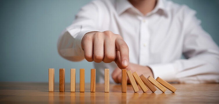 Person pushing dominoes to represent concept of chain reaction cause and effect influence impact strategy planning consequences and leadership in professional environment.