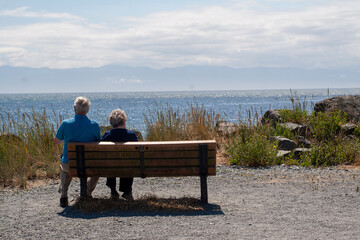 Fototapeta premium Elderly couple sitting on a bench enjoying the ocean view on a sunny day