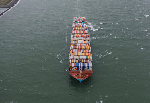Antwerpen, Belgium - 05 September 2019: Aerial view of a massive container ship loaded with colorful cargo navigating the choppy green waters of the Port of Antwerp.
