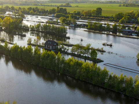 Breukelen, Netherlands - 25 April 2026: Aerial view of Scheendijk islands with small cottages, lush green trees, and calm water under soft sunlight.