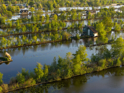 Breukelen, Netherlands - 25 April 2026: Aerial view of Scheendijk featuring narrow land strips with wooden cottages and lush green trees surrounded by the calm waters of Loosdrechtse Plassen.
