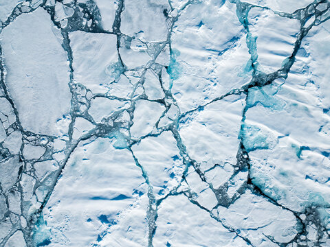Svalbard and Jan Mayen - 01 July 2025: Aerial view of cracked sea ice with intricate fracture patterns and blue water in the Arctic region.