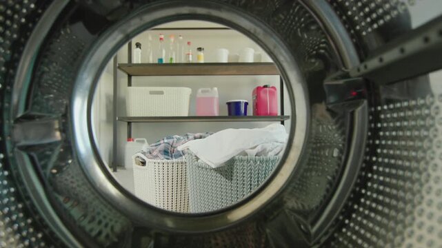 Laundry room view from inside washing machine drum looking out at baskets and shelves.