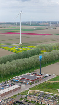 Almere, Netherlands - 17 April 2026: Aerial view of Albert Heijn Oosterwold supermarket with solar panels on the roof, surrounded by wind turbines and colorful tulip fields in the background.