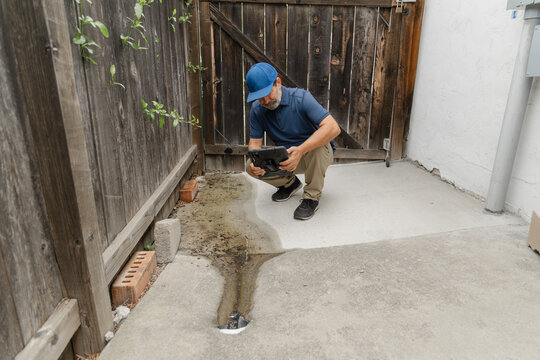 A home inspector checks and takes a pictures of a drainage on the side of a residential home