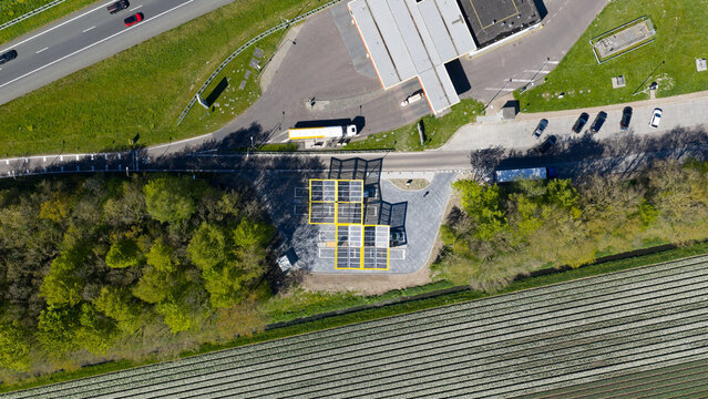 Bant, Netherlands - 21 April 2026: Aerial view of the Fastned charging station with solar panel roofs, located next to a highway and agricultural fields.