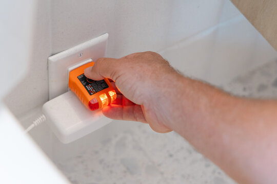 Home inspector using a voltage detector for electrical safety testing on a wall outlet. Non-Contact voltage tester in a hand on a white background