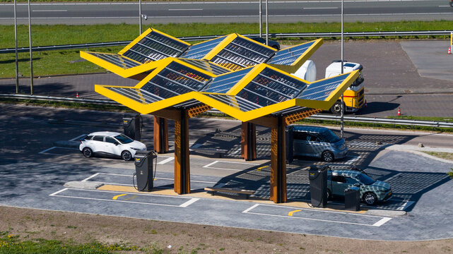 Bant, Netherlands - 21 April 2026: Aerial view of the Fastned Charging Station with its yellow solar-powered roof structure and electric cars parked at charging points near the highway.