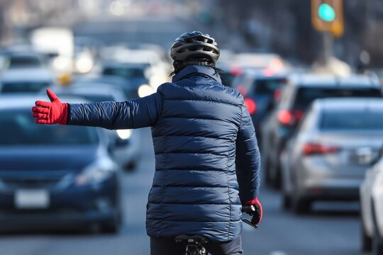 Cyclist in a helmet and warm jacket extends arm with red glove, signaling a turn while navigating urban traffic congestion