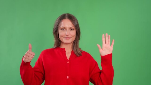 Woman showing the number six with her fingers against a green background while smiling and wearing a red sweater