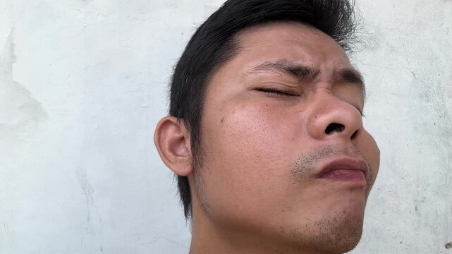 Asian man squinting and making pensive facial expressions outdoors