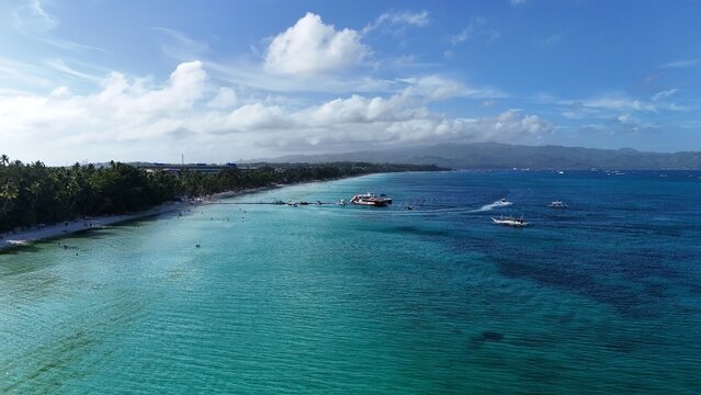 Malay, Philippines - 01 May 2026: Aerial view of Boracay Island featuring turquoise waters, white sand beach, and boats anchored near the tropical shoreline under a cloudy blue sky.