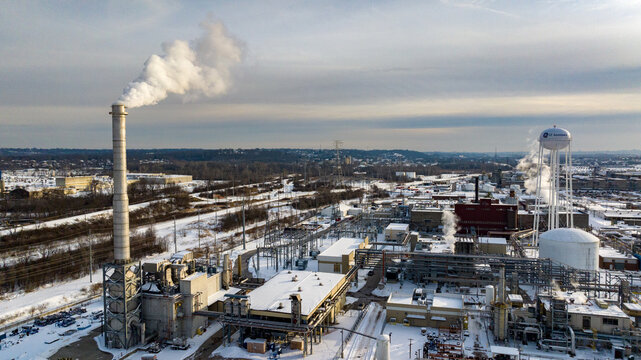 Reading, United States - 29 January 2026: Aerial view of the GE Aerospace industrial facility with a tall smokestack emitting steam over a snow-covered winter landscape.